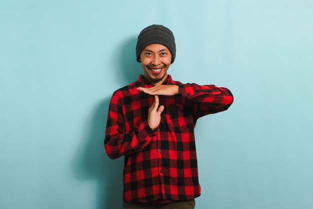 Jovem asiático sorrindo para a câmera enquanto faz um gesto de timeout isolado em um fundo azul