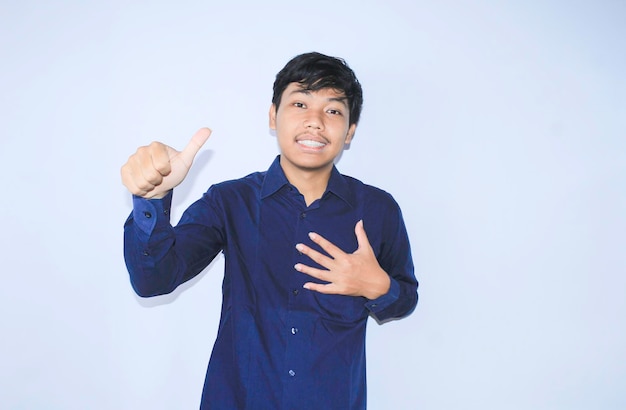 jovem asiático sorrindo sobreviveu de ataque cardíaco está segurando o peito com o polegar para cima usa camisa azul