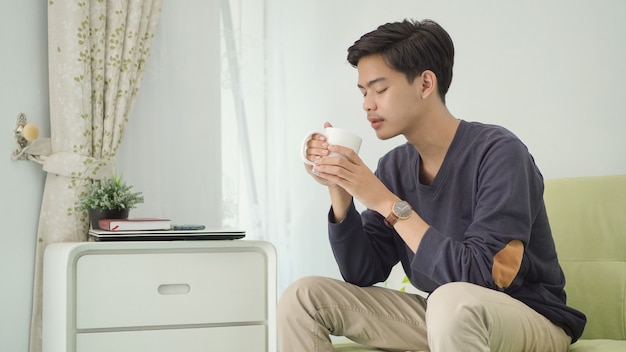 Jovem asiático tomando uma bebida em casa depois do trabalho