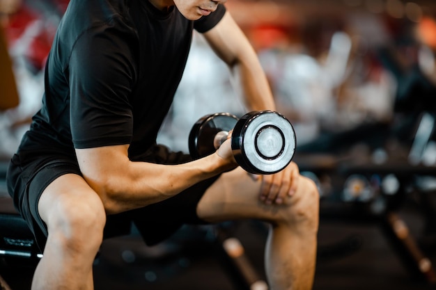 Jovem asiático usando exercícios com halteres na academia para uma boa saúde em fitness estilo de vida e conceito de exercício esportivo