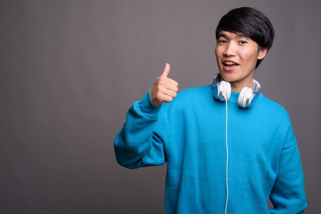 Jovem asiático usando fones de ouvido contra uma parede cinza