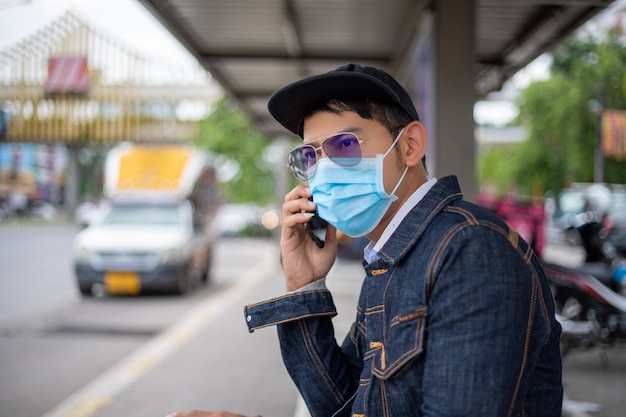 Jovem asiático usando telefone inteligente na cidade e usando máscara facial para proteção da poluição do ar, partículas e proteção contra vírus da gripe, influenza, coronavírus