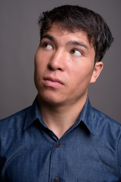 Jovem asiático vestindo camisa azul contra uma parede cinza