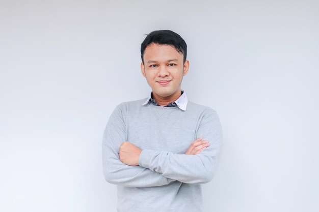 Jovem asiático vestindo camisa branca está de mãos cruzadas com sorriso feliz e confiança Homem indonésio bem sucedido em fundo cinza