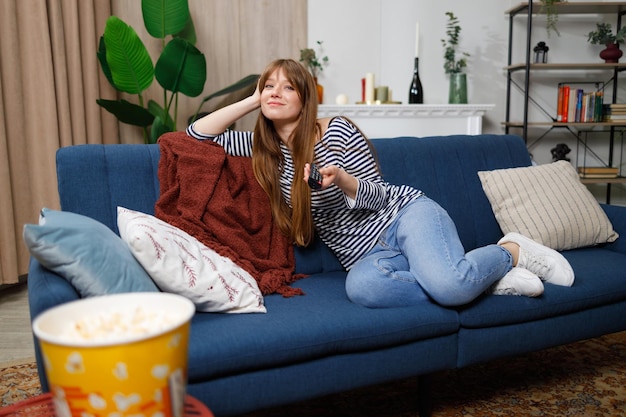 Jovem assistindo tv e usando o controle remoto no sofá em casa