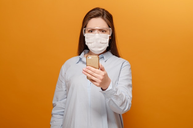 Jovem assustada com máscara médica no rosto olha para telefone, mulher em pânico por epidemia