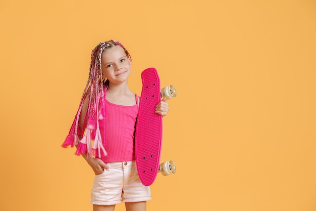 Jovem ativa com dreadlocks na camisa rosa e shorts com pennyboard sobre fundo amarelo