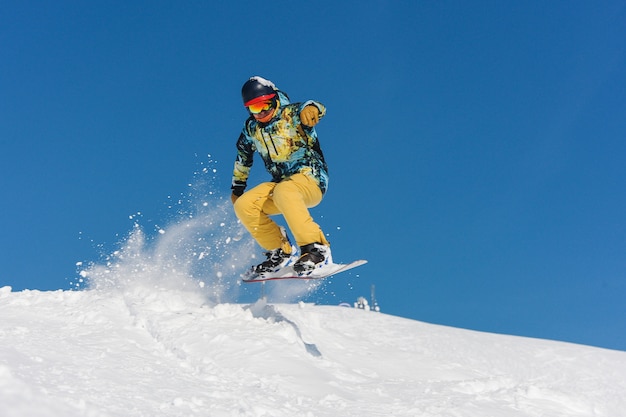 Jovem ativo snowboarder no sportswear brilhante pulando na encosta de uma montanha