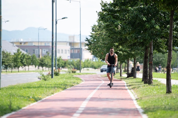 Jovem atleta atraente está dirigindo sua scooter na rua no dia ensolarado