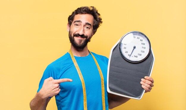 Jovem atleta barbudo louco apontando ou mostrando e conceito de dieta e segurando uma balança