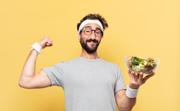 Jovem atleta barbudo maluco com expressão feliz e segurando uma salada