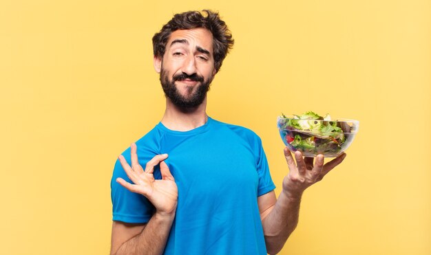 Jovem atleta barbudo maluco com uma expressão feliz segurando uma salada