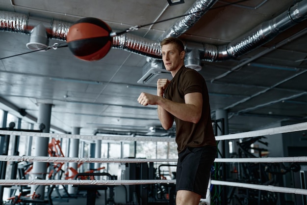 Jovem atleta boxer forte lutador treinando com saco de pancadas no ringue de ginástica se preparando para o treinamento