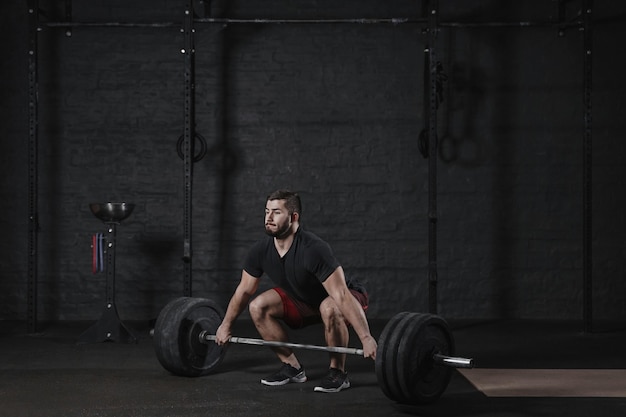 Jovem atleta de crossfit fazendo exercício de levantamento terra com barra pesada na academia Homem praticando treino funcional de levantamento de peso