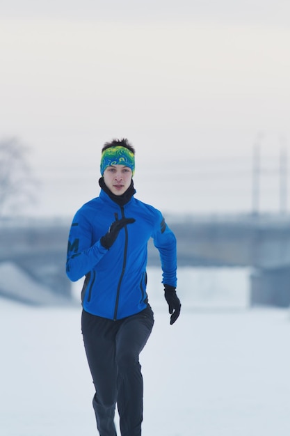 Jovem atleta do sexo masculino correndo no inverno através do conceito de neve, esporte e lazer