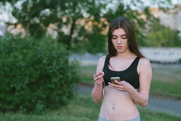 Jovem atleta em uma camisa curta com uma bela figura usa um telefone celular