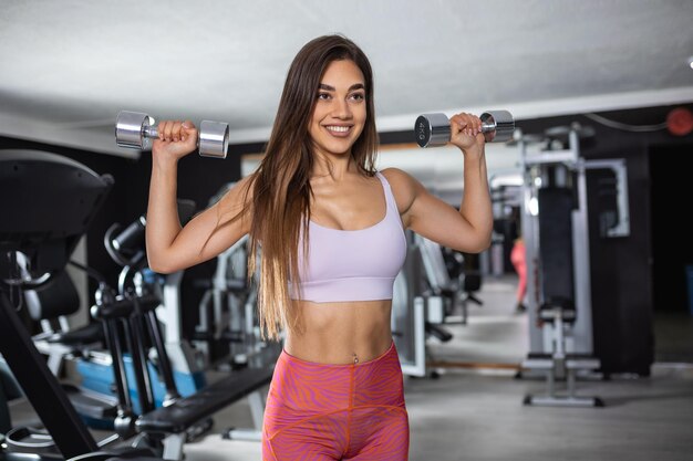 Jovem atleta feminina fazendo exercícios de força com peso de mão em uma academia Desportista exercitando com halteres durante treinamento esportivo em uma academia