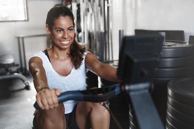 jovem atleta motivada, sorrindo na academia, usando equipamento de leg press