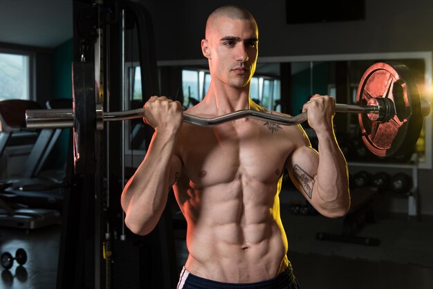 Jovem atleta no ginásio realizando roscas de bíceps com uma barra
