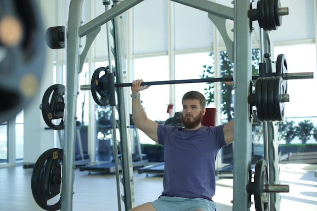 Jovem atlético está treinando na academia fazendo exercícios com barra