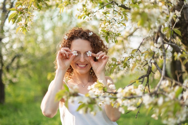 Jovem atraente caminha no parque verde primavera, apreciando a natureza de floração. Menina sorridente saudável girando no gramado da primavera. Alergia sem