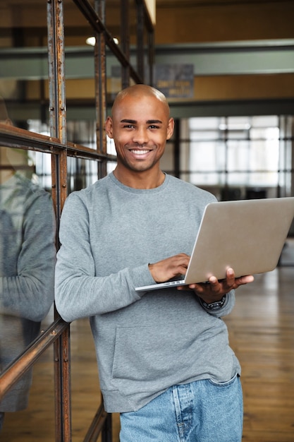 jovem atraente careca afro-americano vestindo um moletom segurando um laptop enquanto trabalhava no escritório