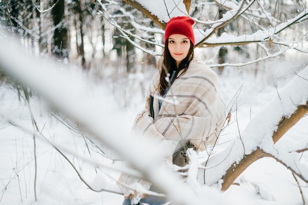 Jovem atraente cobrindo uma capa quente posando entre galhos de neve