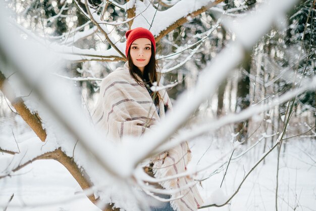 Jovem atraente cobrindo uma capa quente posando entre galhos de neve