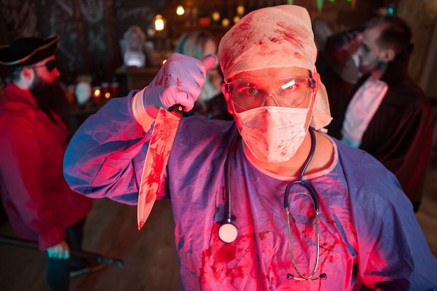 Jovem atraente com uma fantasia de médico segurando uma faca na festa de halloween. Vida noturna de Halloween.