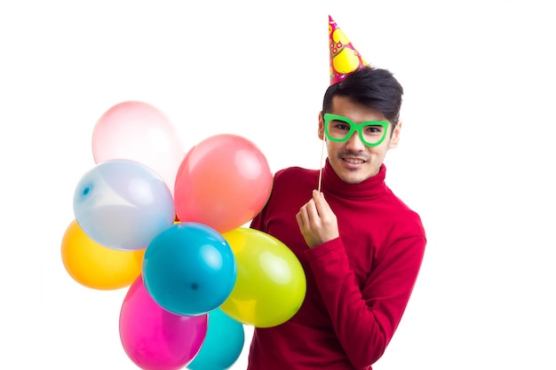 Jovem atraente de camisa vermelha com chapéu comemorativo segurando muitos balões coloridos no estúdio