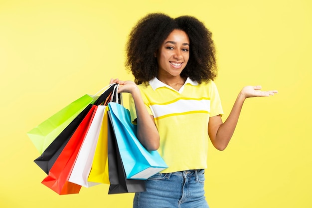 Jovem atraente e feliz mulher afro-americana segurando sacolas coloridas isoladas em amarelo