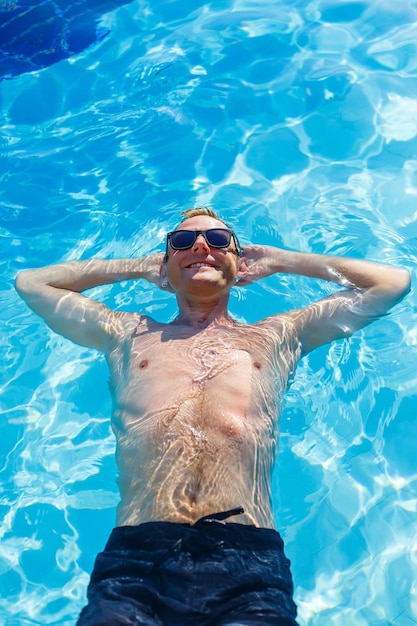 Foto jovem atraente em óculos de sol está descansando na piscina nas férias de verão. o cara na piscina do hotel