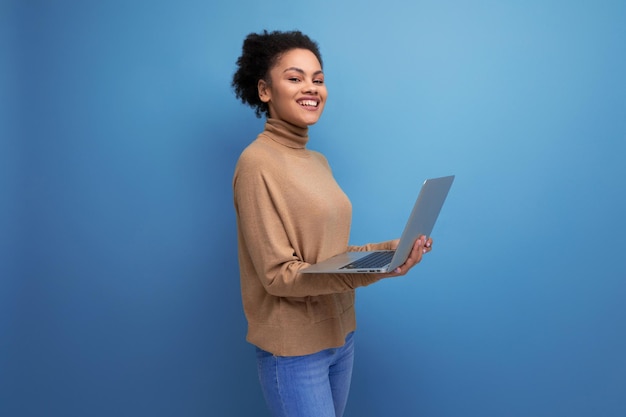 Jovem atraente estudante latina com rabo de cavalo afro preto segurando laptop