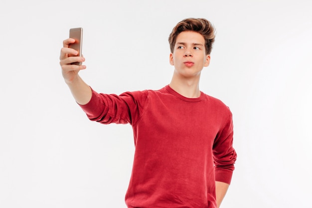 Jovem atraente faz uma selfie com smartphone em branco bac