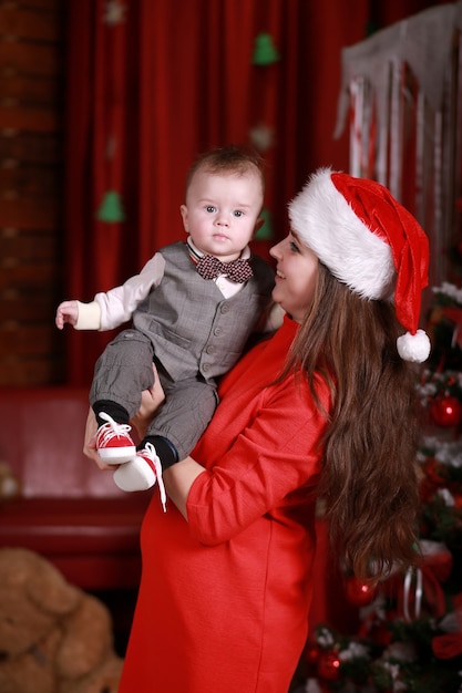 Jovem atraente feliz mãe com chapéu de Papai Noel se divertir com seu filho em casa perto da árvore de Natal. Família, felicidade, feriados, conceito de ano novo