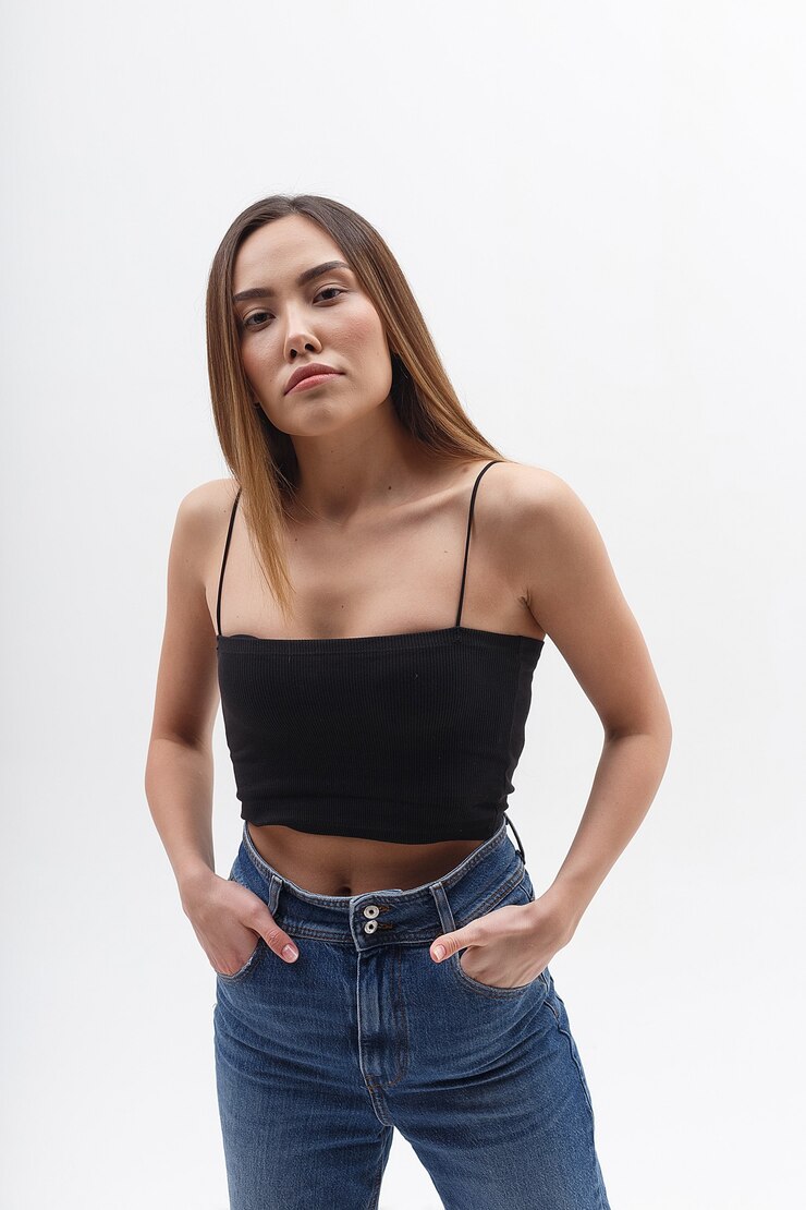 Foto jovem atraente mulher asiática com cabelo comprido em jeans azul, top preto, isolado na parede branca. magricela muito feminina posando no ciclorama com as mãos nos bolsos. testes de modelo de bela senhora