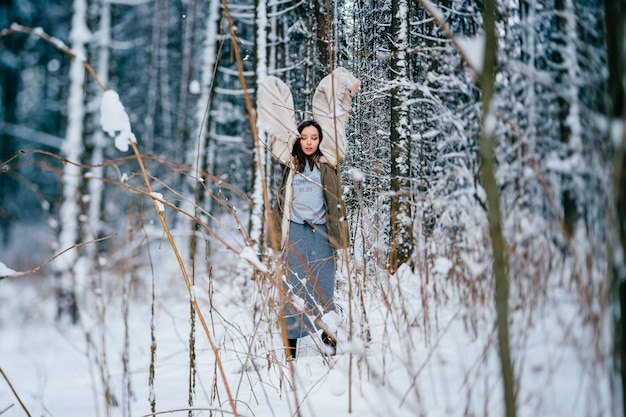 Jovem atraente posando com uma capa quente entre as árvores na floresta de neve