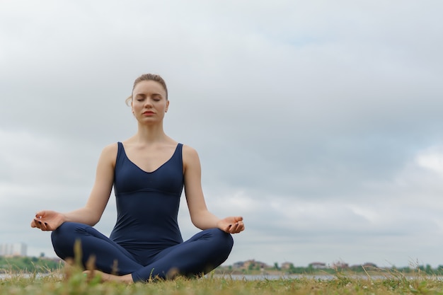 Jovem atraente praticando ioga sentada em pose de ardha padmasana de meio exercício de lótus