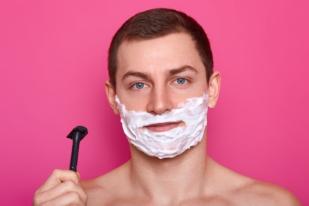 Jovem atraente pronto para fazer a barba com navalha no banheiro