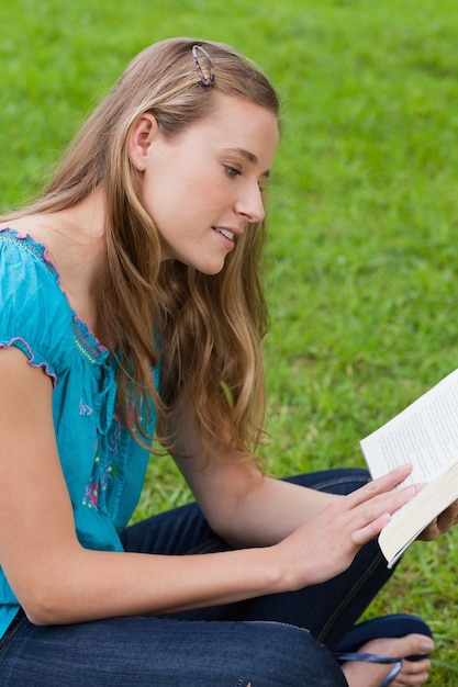 Jovem atraente sentada de pernas cruzadas em um parque enquanto lê um livro