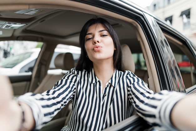 Jovem atraente, sentado em um carro, fazendo uma selfie em seu telefone