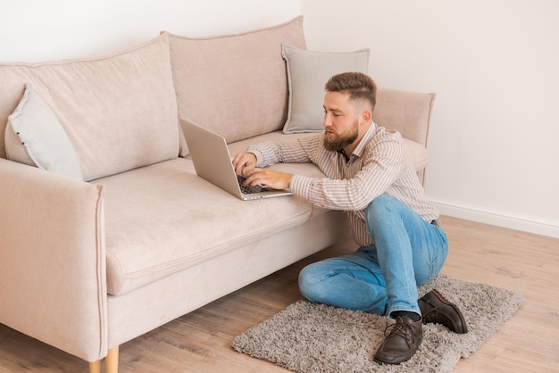 Jovem atraente sentado no sofá em casa trabalhando no laptop online usando