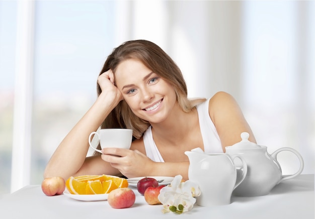 Jovem atraente tomando chá e frutas no café da manhã