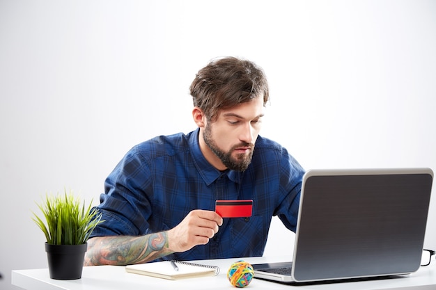 Jovem atraente vestindo camisa azul, sentado com o laptop, conceito de compras online, retrato, compras online móvel.