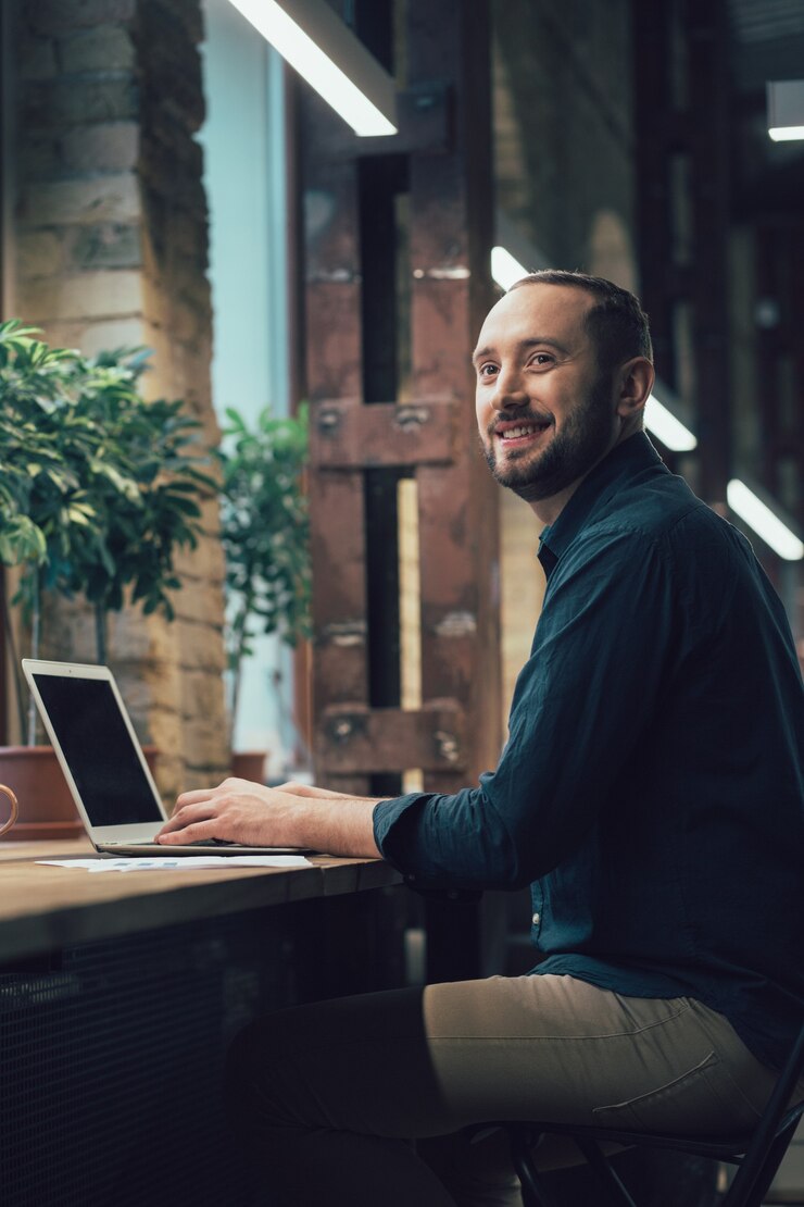 Jovem atraente virando a cabeça e olhando para longe com um sorriso enquanto está sentado com um laptop moderno