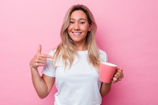 Jovem australiana segurando uma caneca rosa isolada em um fundo rosa pessoa apontando com a mão para um espaço de cópia de camisa, orgulhosa e confiante