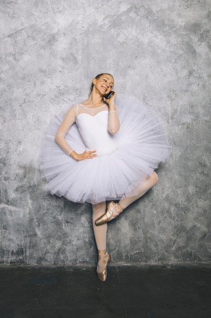 Foto jovem bailarina bailarina clássica usando telefone celular contra parede rústica