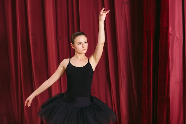 Jovem bailarina de vestido preto treina nos bastidores.