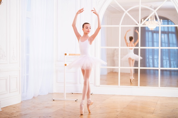 Foto jovem bailarina em pé na ponta de um tutu em um belo corredor branco em frente ao espelho.