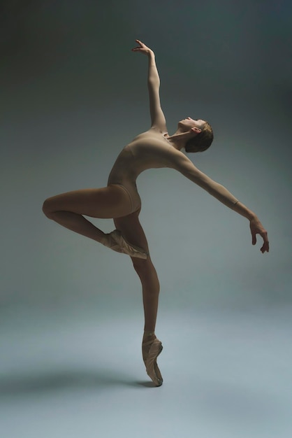 jovem bailarina em um estúdio de fotos em um bodysuit e sapatos de ponta mostra movimentos de ballet